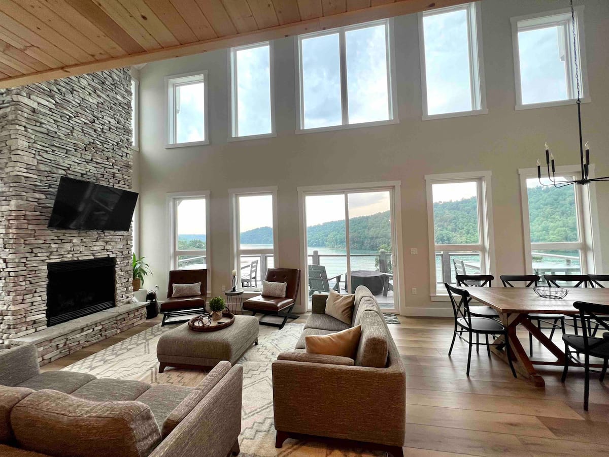 Modern lake cottage living room with vaulted ceilings, stone fireplace, and floor-to-ceiling lake windows